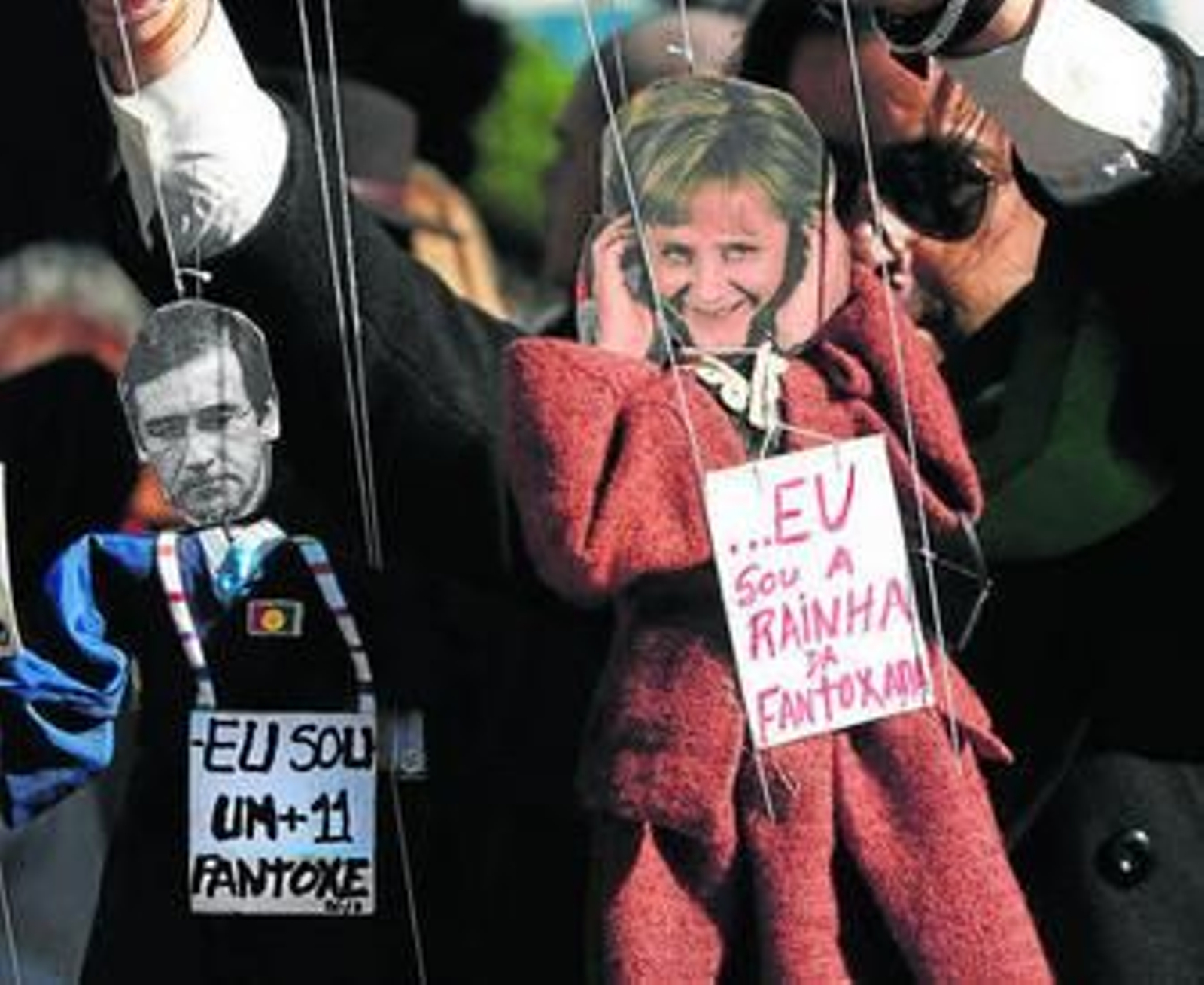 Un hombre sujeta dos marionetas de la canciller Angela Merkel, y el primer ministro portugués, Passos Coelho.