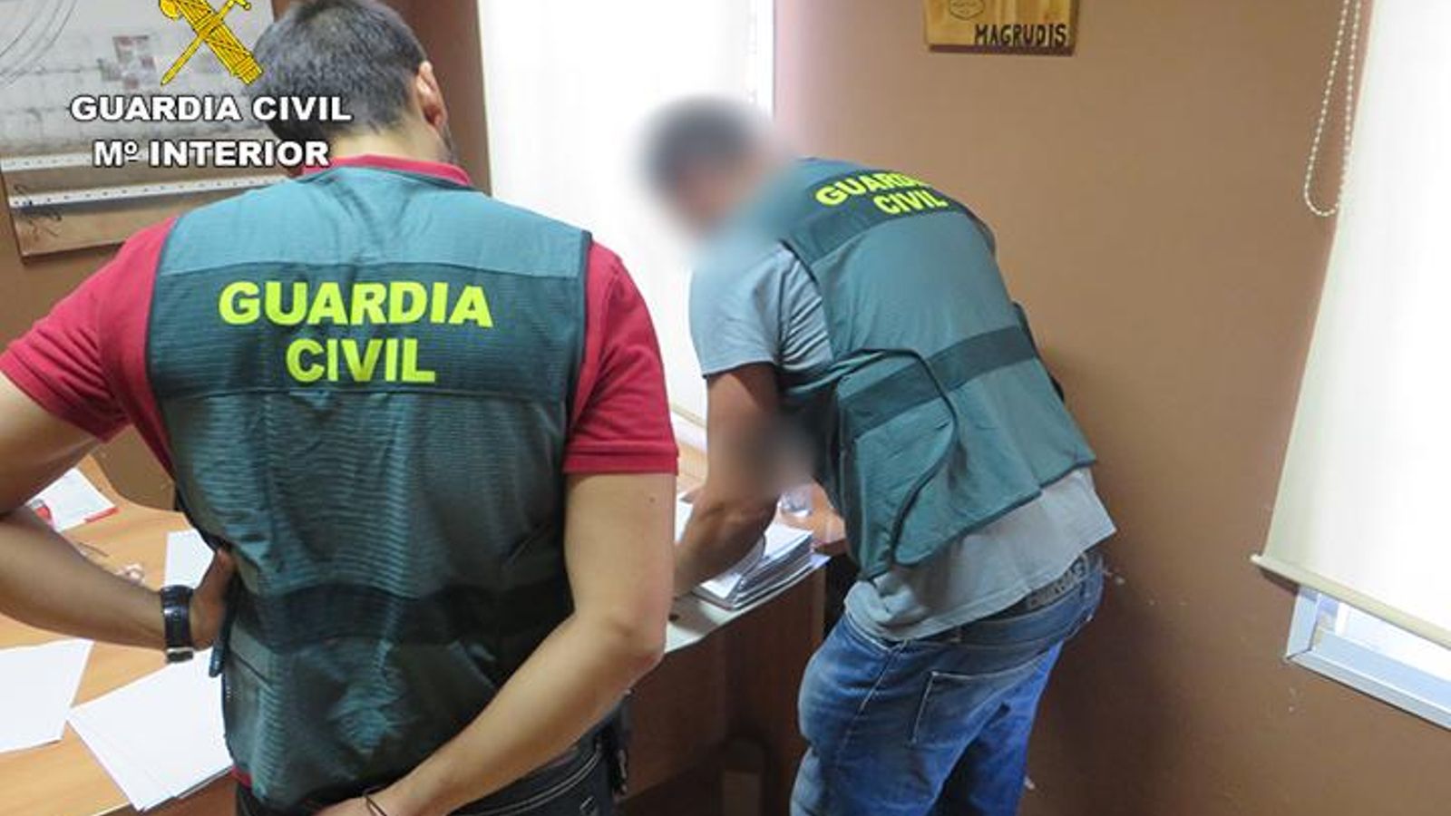 Varios agentes examinan documentación en la fábrica con un cartel al fondo de la marca "La Mechá"