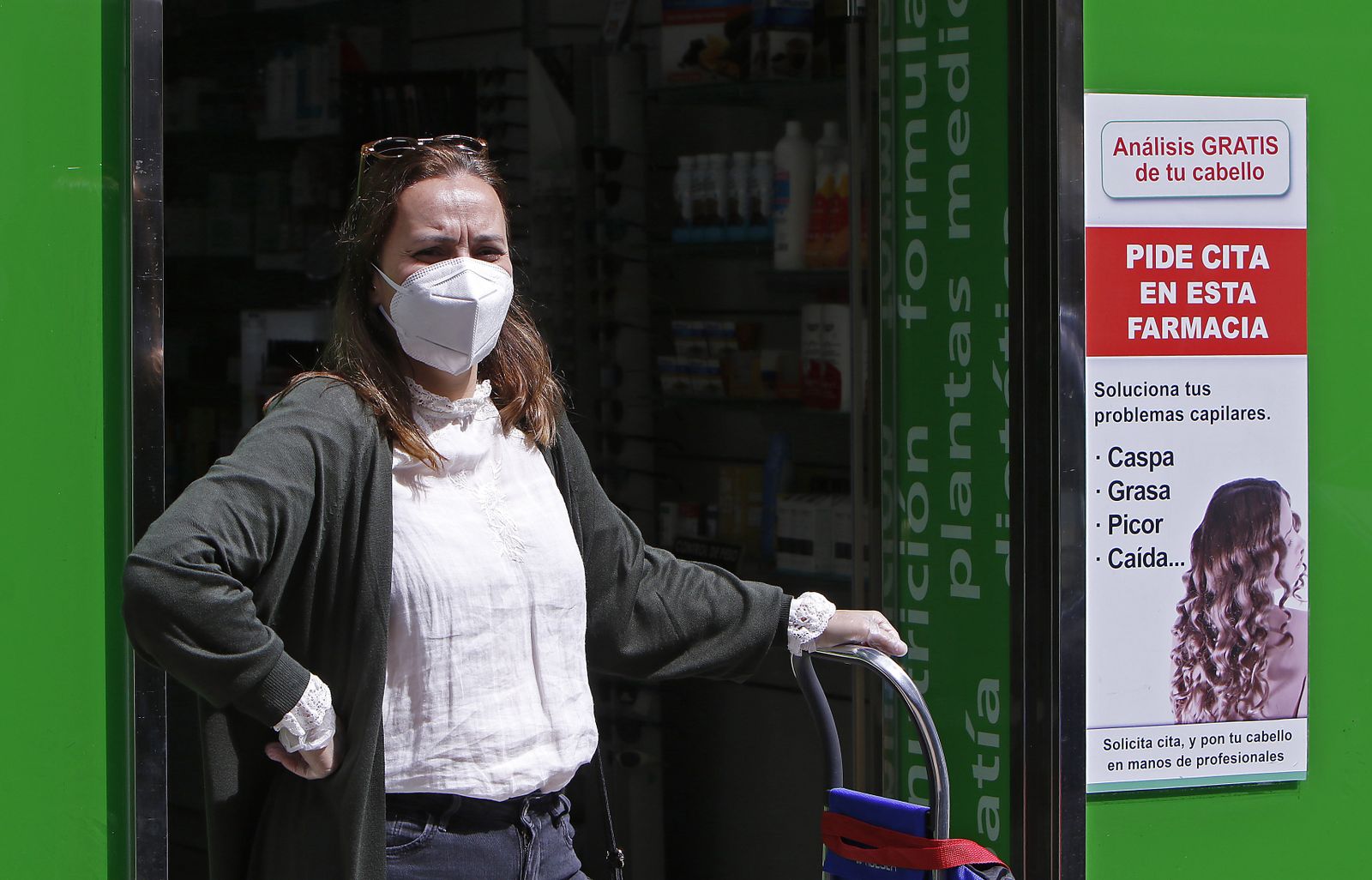Una mujer con mascarilla en la puerta de una farmacia.