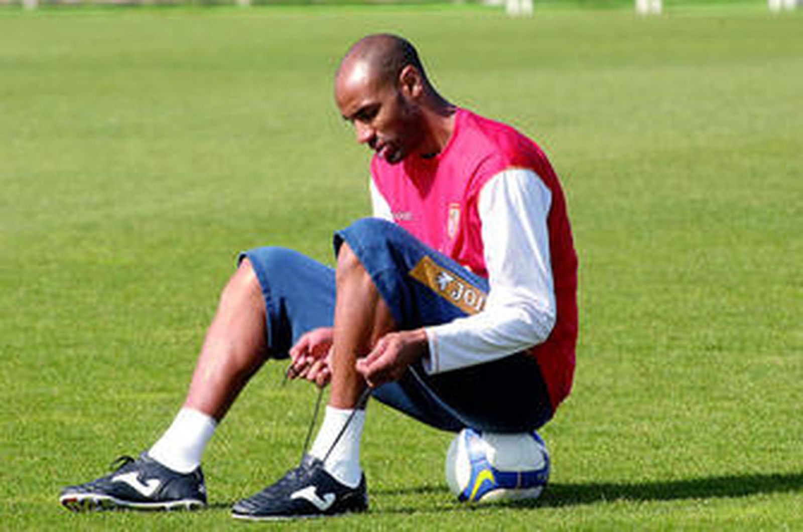Frederic Kanoute se amarra las botas sentado en un balón durante el entrenamiento.