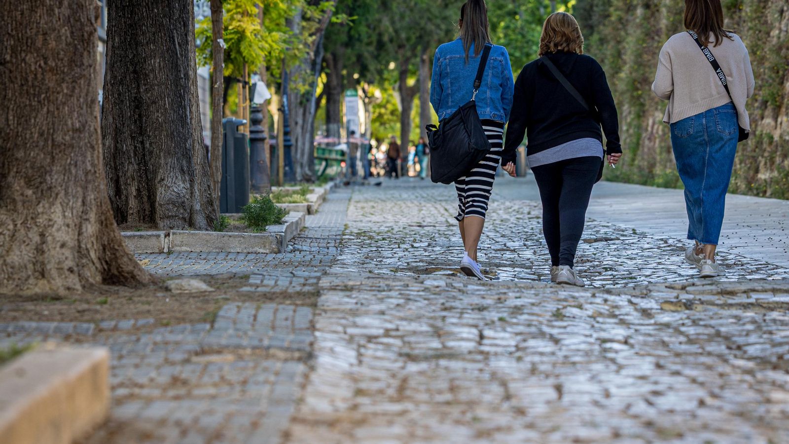 Tres mujeres caminan por el deteriorado adoquinado de esta vía.