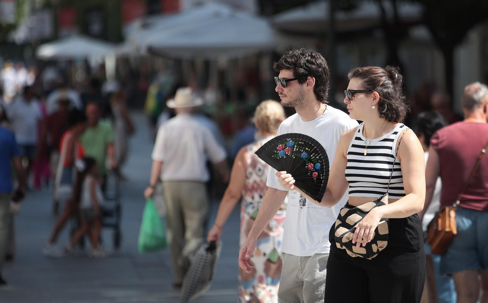 Una mujer se abanica mientras camina acompañada en una calle del centro de Jerez
