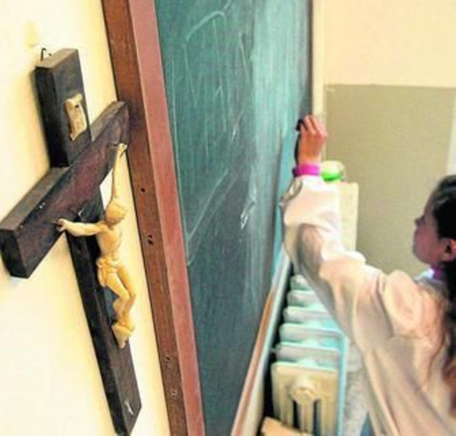 Crucifijo situado junto a una pizarra en la que escribe una alumna.