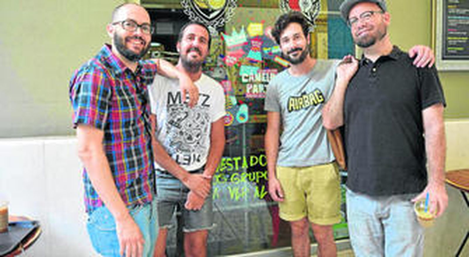 Los organizadores del Festival 'Canela Party' posan frente al cartel, exhibido desde hace unos días en la facha de la cafetería El Último Mono.