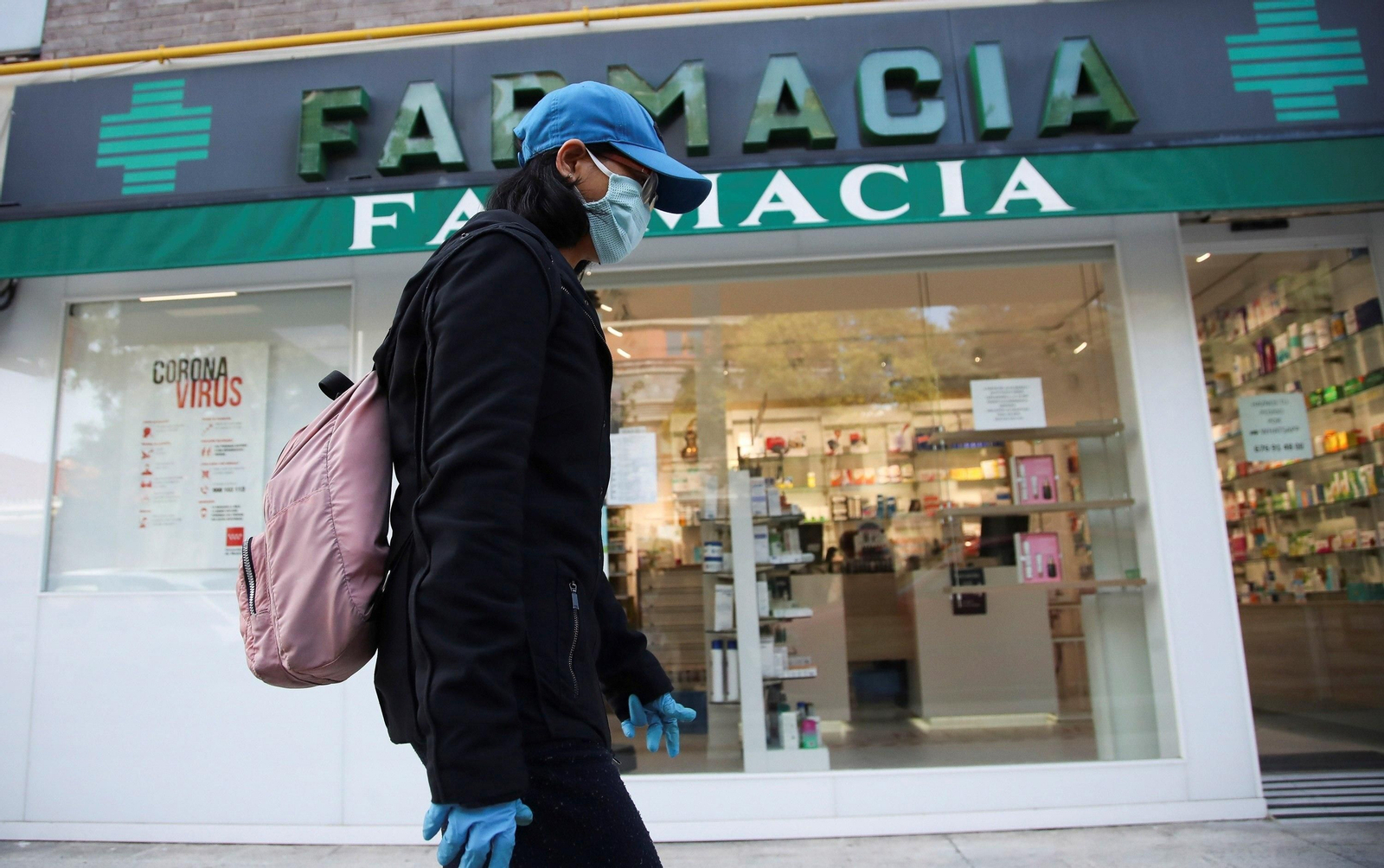 Una viandante, con mascarilla, pasa por delante de una farmacia.