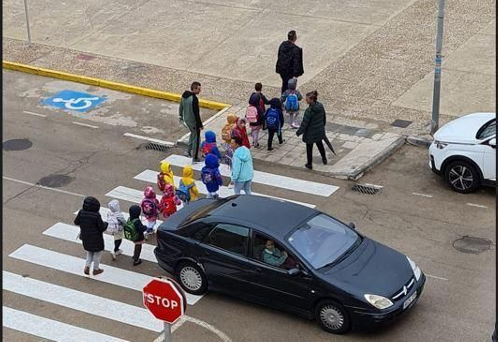 Niños cruzan bajo la lluvia un paso de peatones ocupado por un coche, este miércoles
