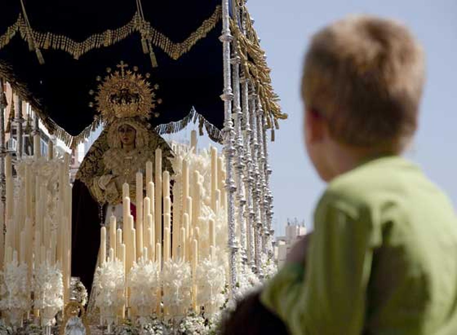 El Palio de la Hermandad del Polígono San Pablo es contemplada por un menor en las calles del barrio sevillano.

Foto: Jaime Martínez
