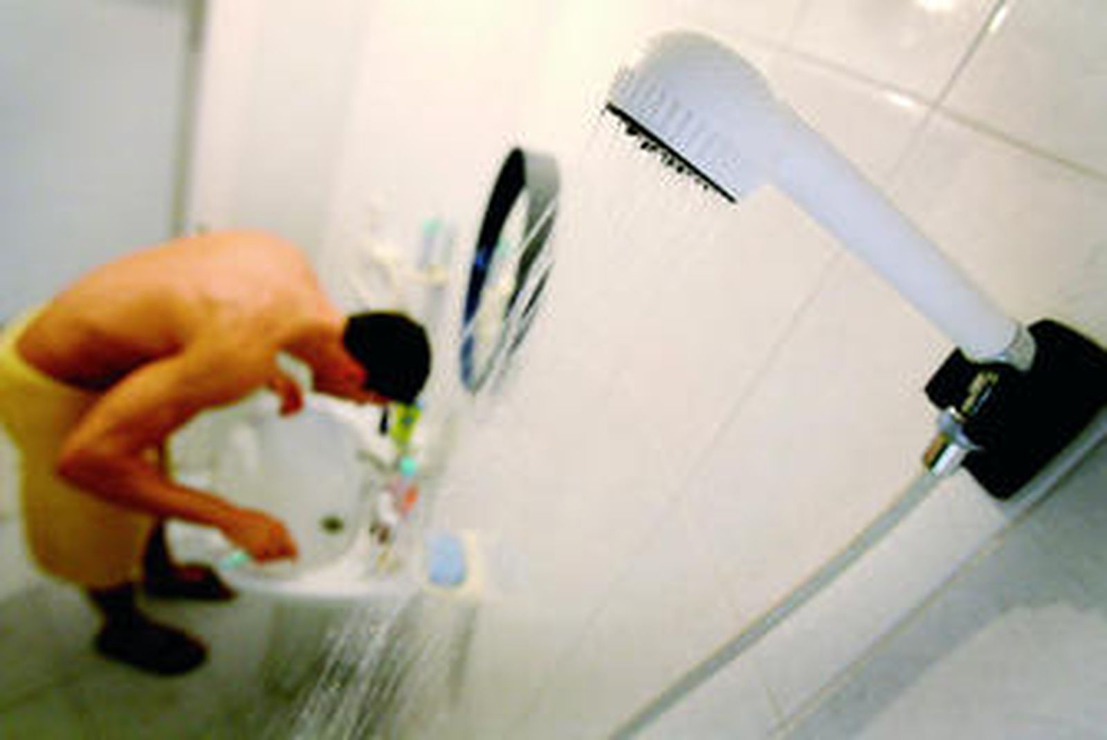 Un joven se lava los dientes mientras mantiene el grifo de la ducha abierto.