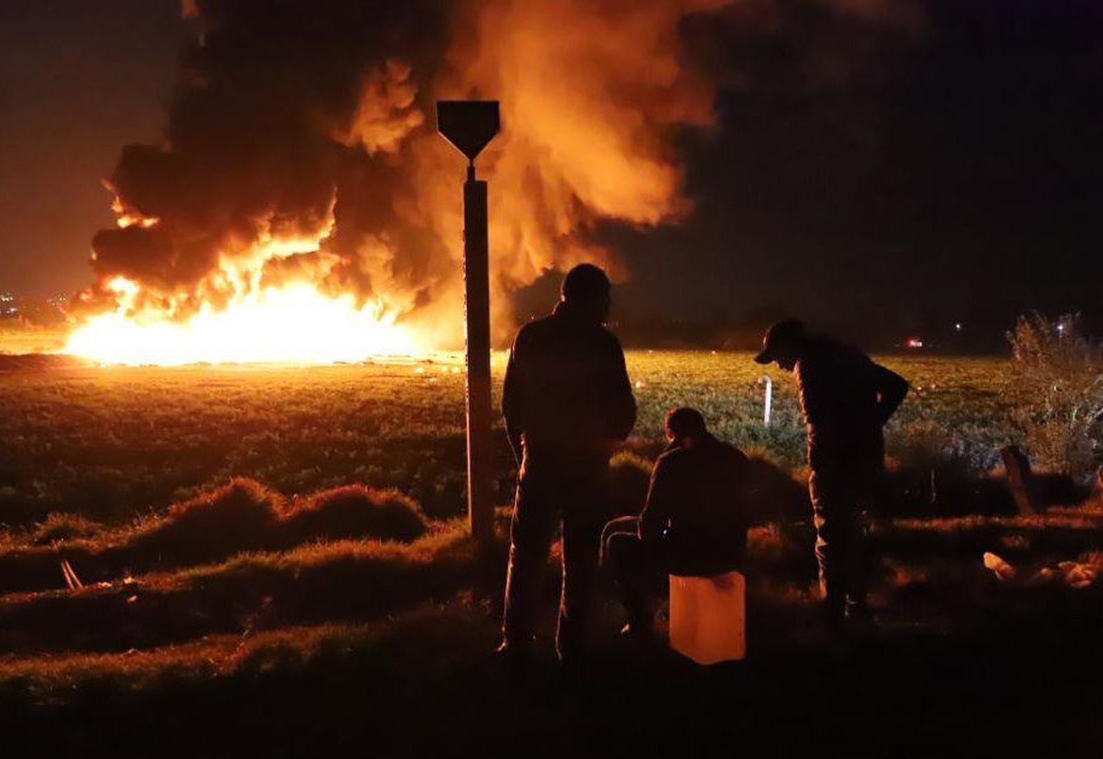 Tres personas observan el fuego sobre un bidón vacío.