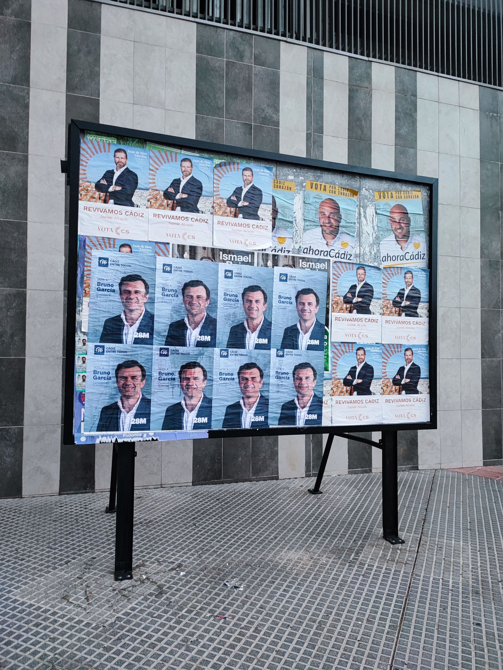 Carteles de Bruno García (PP) y de Eugenio Belgrano (Ahora Cádiz) sobre los de Juan de Dios Sánchez, en el panel de Cs.