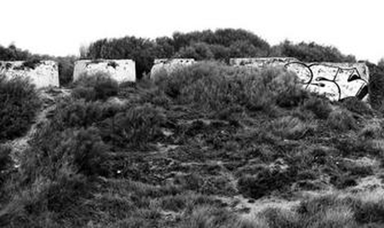 La deteriorada batería de las Arenillas, junto a la playa de Las Redes, cubierta de vegetación, arena y pintadas.
