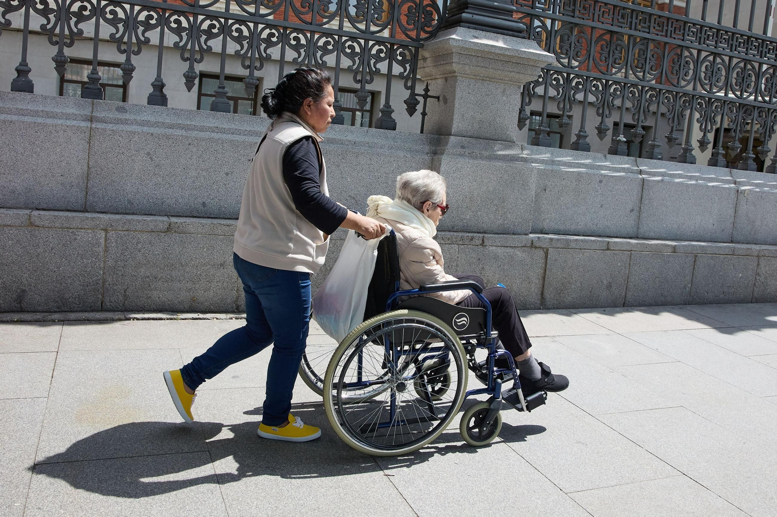 Una cuidadora empuja una silla de ruedas de una persona mayor
