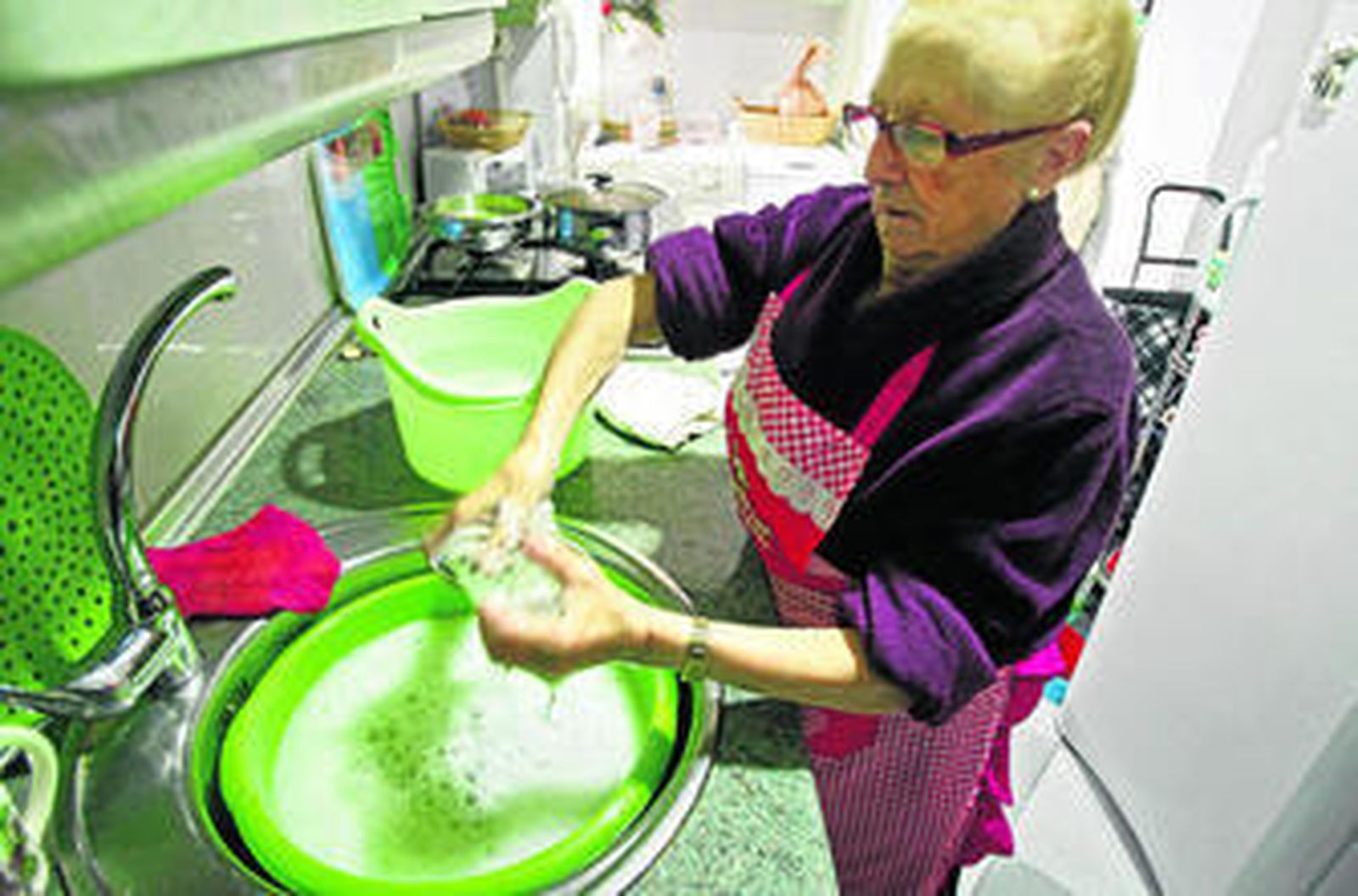 Ángeles Santantón, vecina del barrio de Loreto, friega los platos y los vasos en dos barreños para enjabonar y enjuagar.