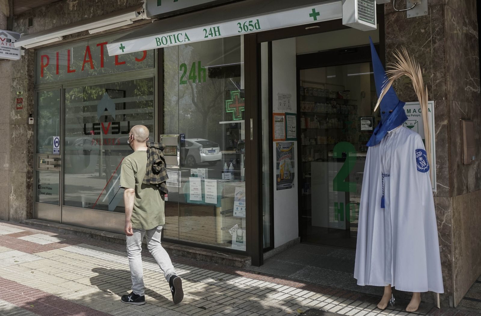 Un hombre pasa por una botica con una túnica de nazareno en el exterior del negocio.