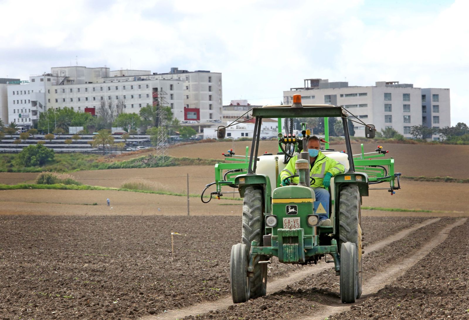 Preparación de las tierras para la siembra en una explotación de Jerez con el hospital al fondo.