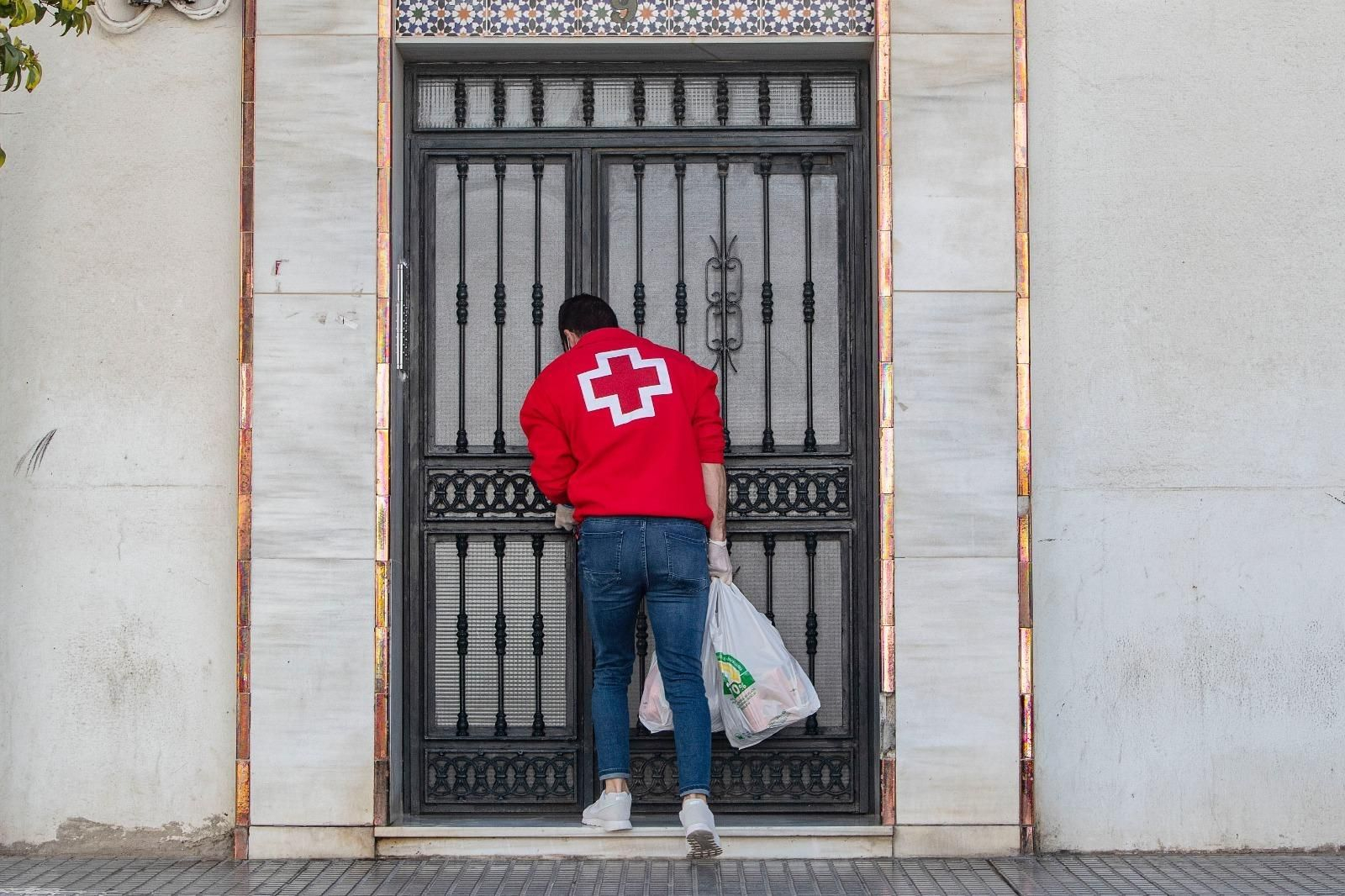 Un voluntario de Cruz Rojas con bolsas de la compra en la puerta de un domicilio.