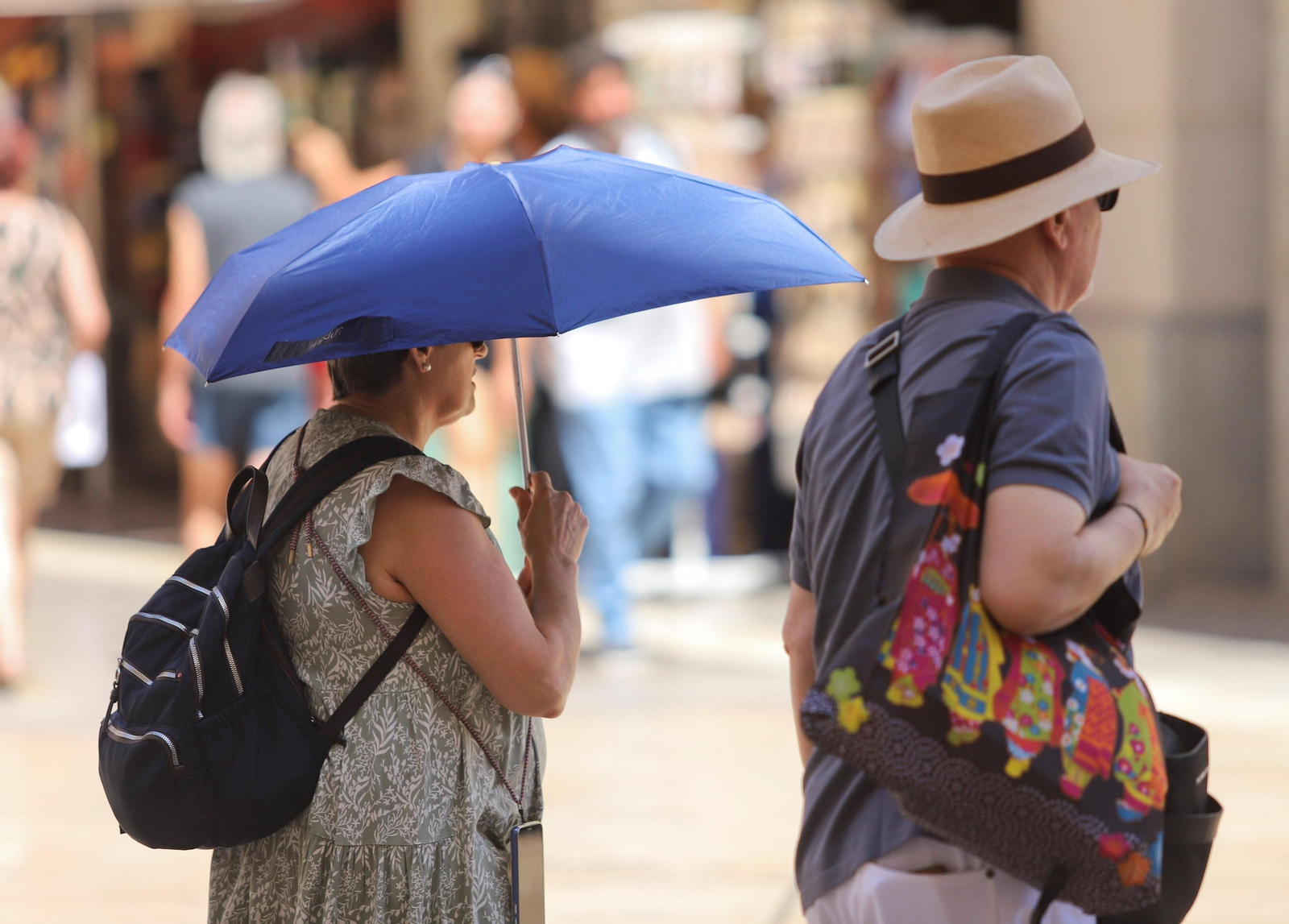 Dos personas caminan por una calle de Málaga resguardándose del calor. Dos personas caminan por una calle de Málaga resguardándose del calor.