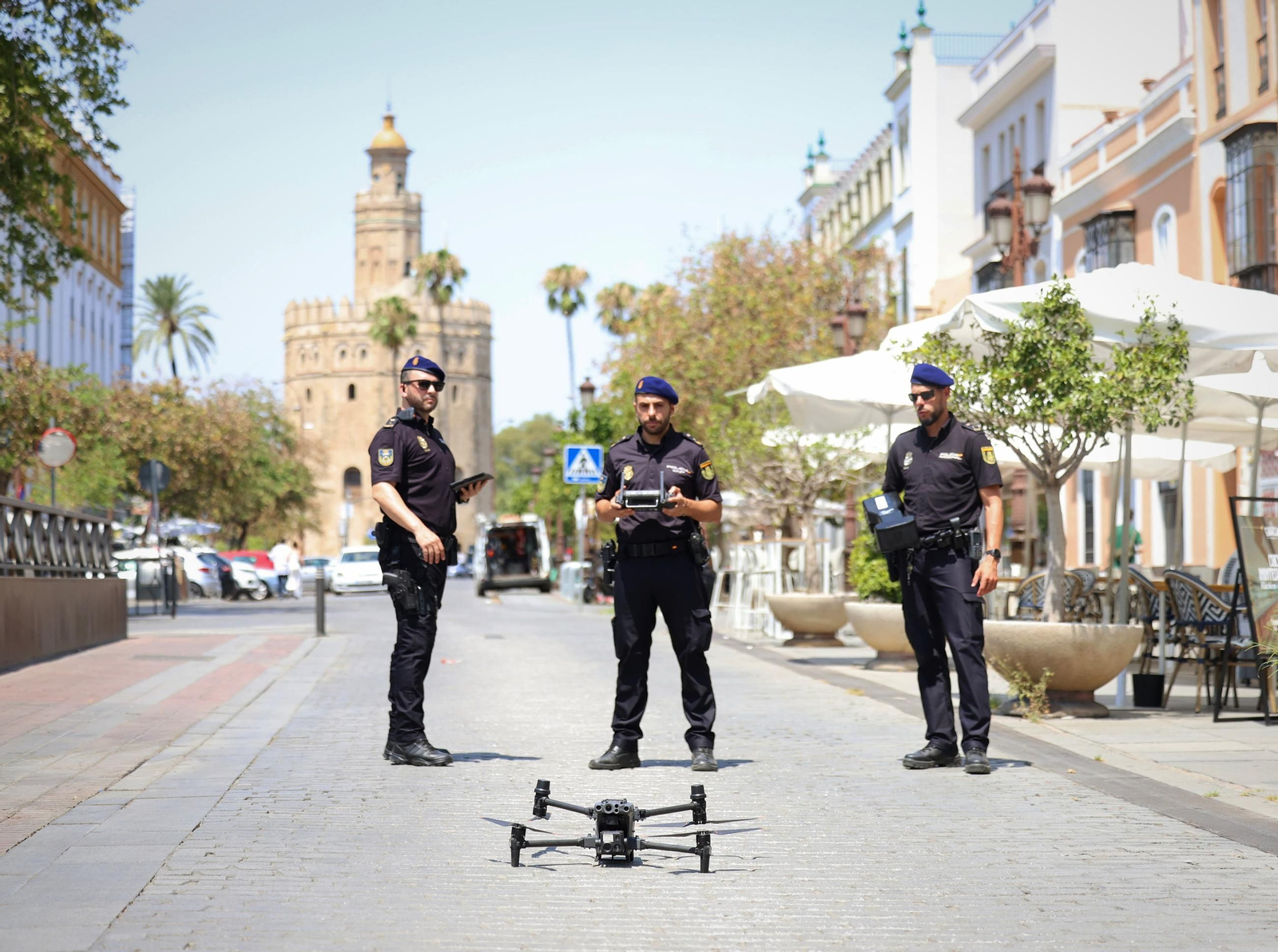 Tres policías con un dron con la Torre del Oro al fondo.