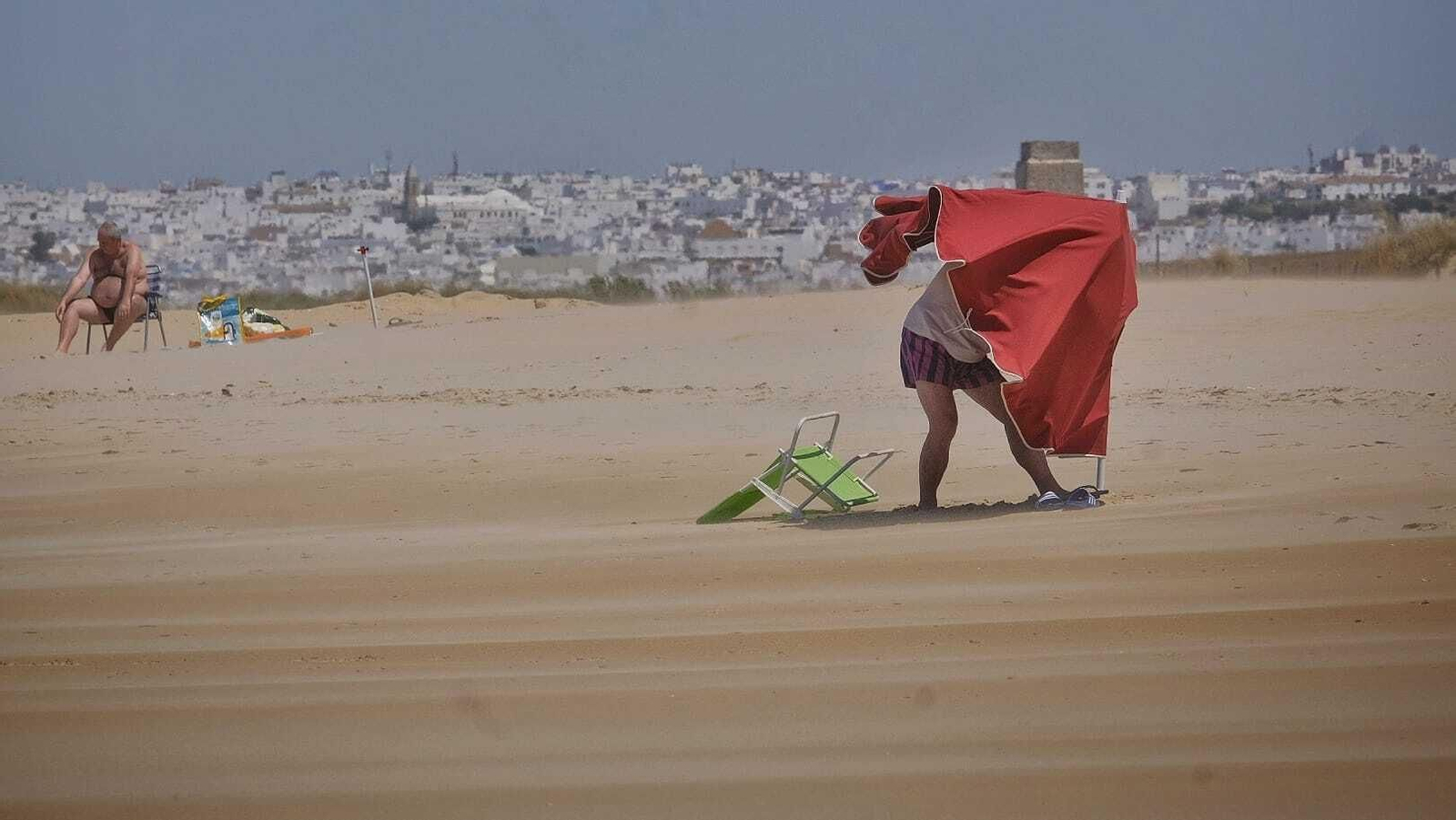 Una persona intentando poner una sombrilla en El Palmar este lunes.