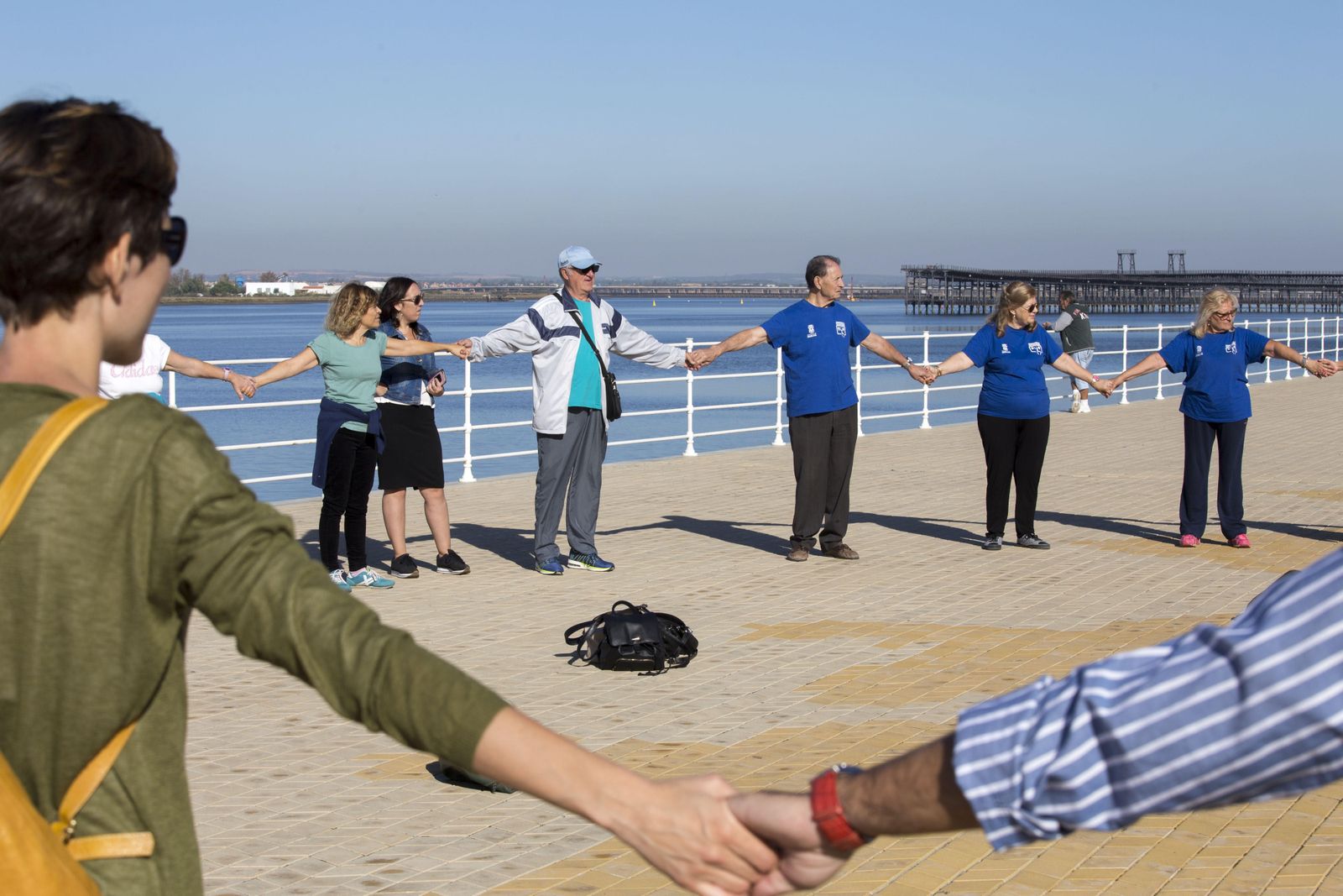 1. Los participantes del paseo saludable realizan una actividad en el Paseo de la Ría. 2. Los 50 onubenses que participaron utilizaron ropa cómoda y deportiva para recorrer el camino programado. 3. Dos señoras realizan una actividad en el Paseo de la Ría. 4. Tres de los participantes durante el recorrido del ejercicio enmarcado en la programación del Mes del Mayor. 5. Foto de familia de todos los integrantes que participaron en el paseo saludable.