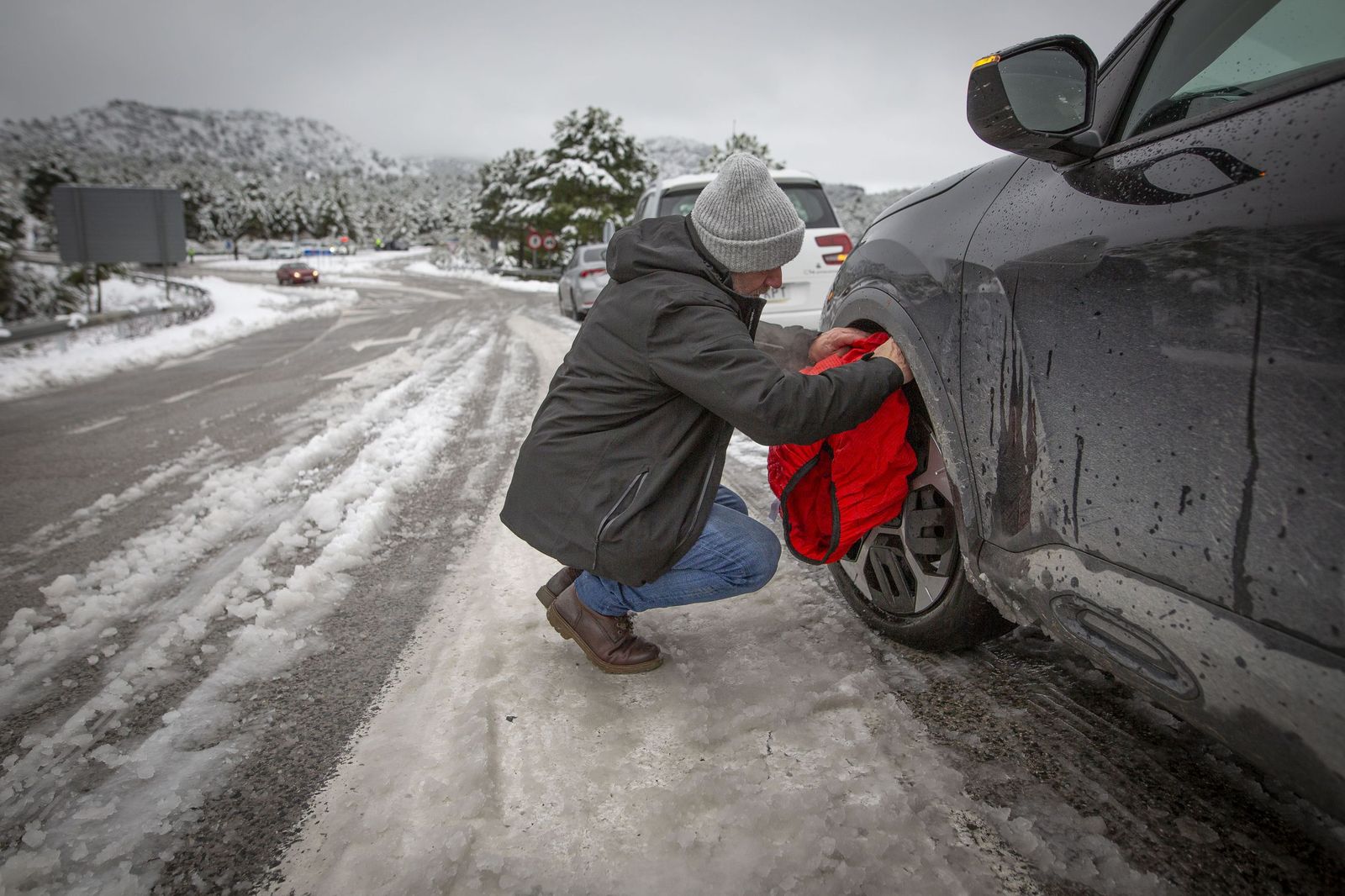 Un hombre coloca mantas de invierno en su coche para poder pasar por la zona de la nieve caída este lunes en Granada