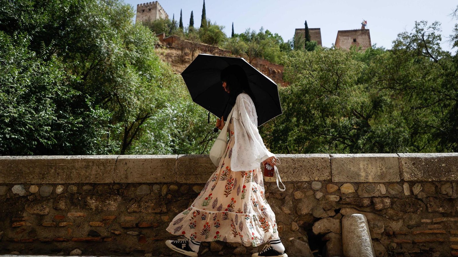 Una joven se protegen de los rayos del sol frente a la Alhambra de Granada