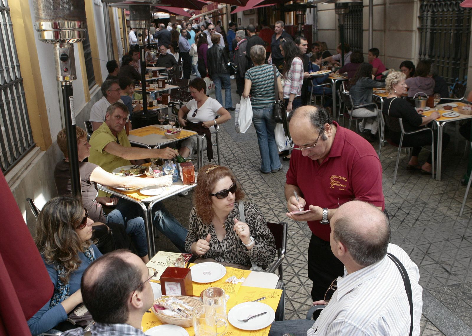 Un camarero atiende una mesa en una popular calle llena de bares en el centro de Sevilla.