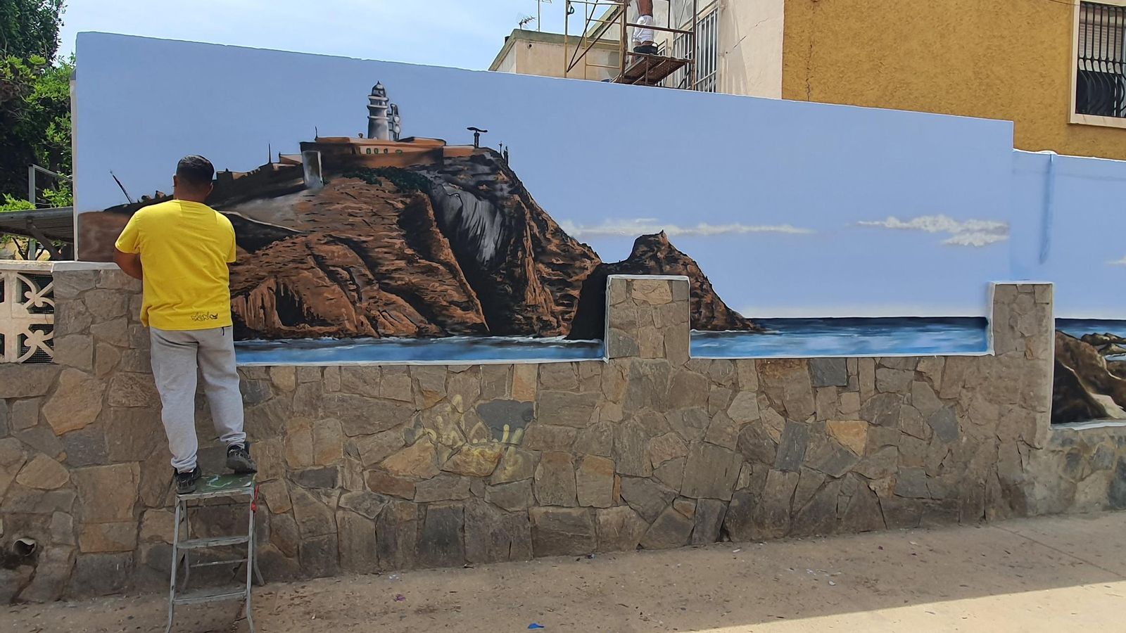 Uno de los artistas pinta el peñón donde está instalado el Faro de Cabo de Gata.