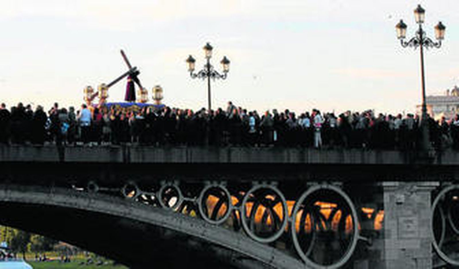 Jesús Nazareno, siempre agobiado con su cruz, cruza el puente de Triana hacia Sevilla,  en el atardecer del Viernes Santo.
