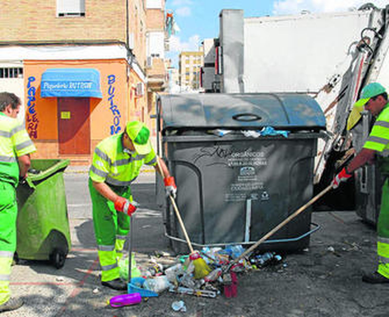 Trabajadores del servicio de recogida de basura limpian alrededor de un contenedor.