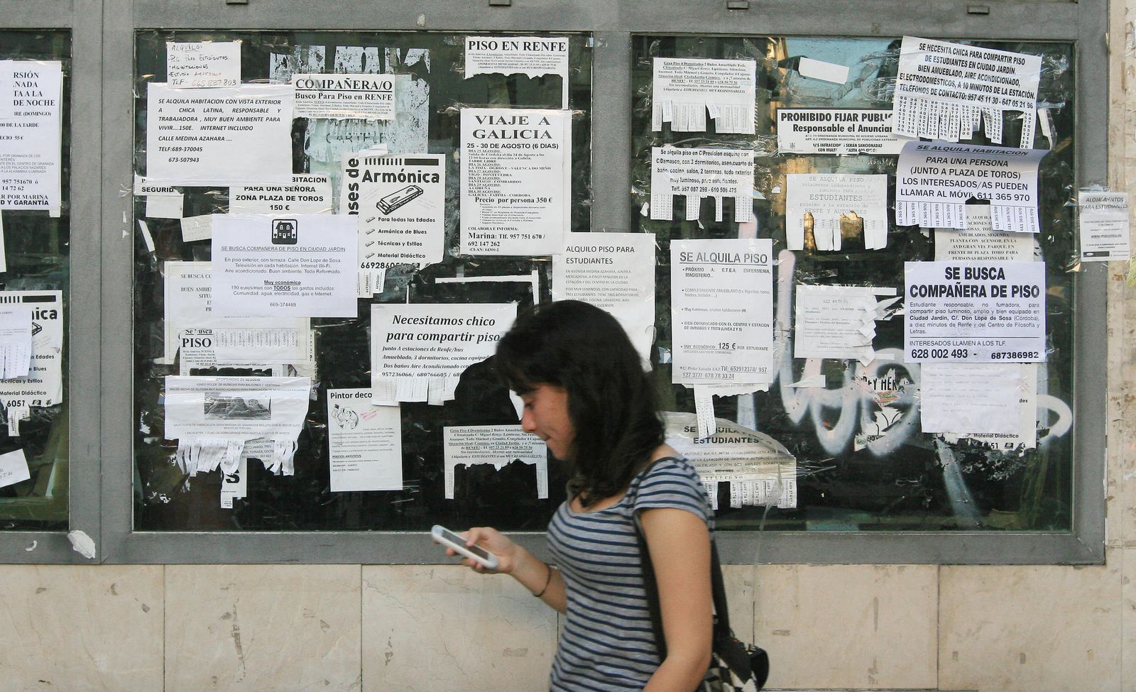 Una mujer pasa por delante de un gran número de carteles anunciadores de pisos de alquiler.