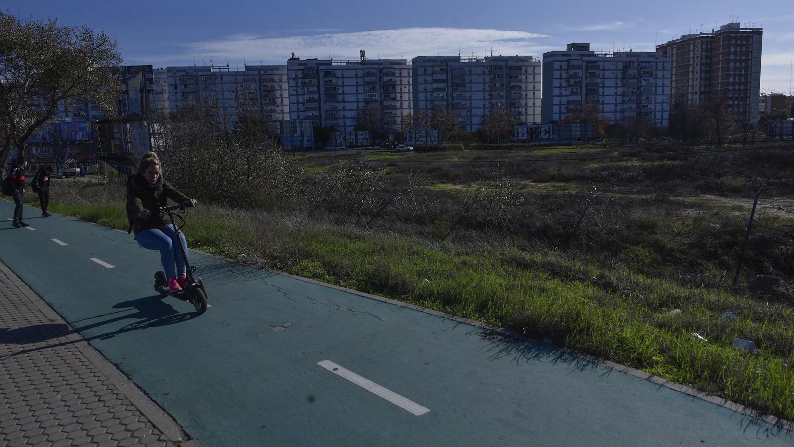 Una joven circula con un patinete eléctrico por un carril bici que linda con la parcela.