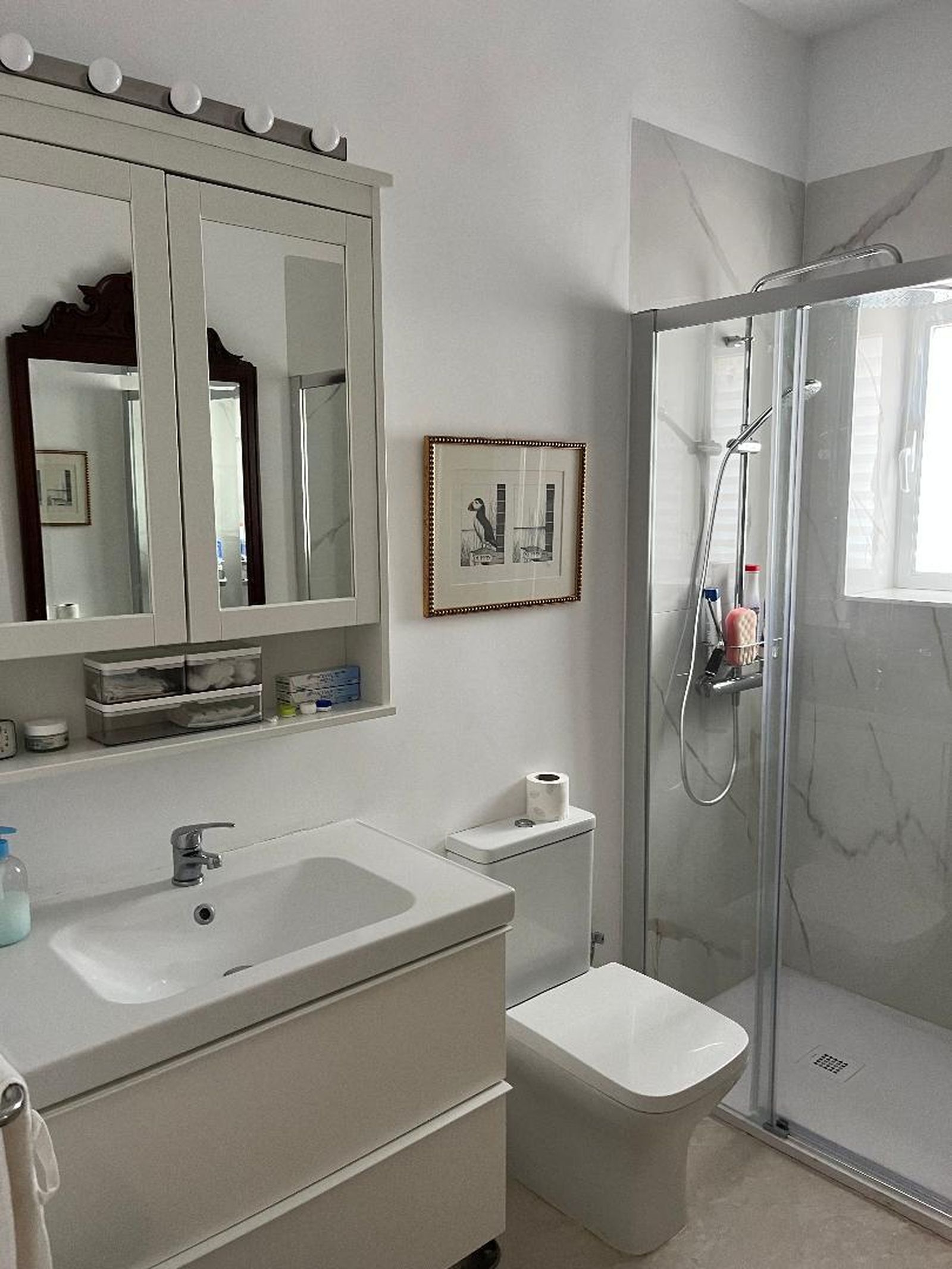 El blanco de las paredes del baño se combina con el mármol de su ducha.