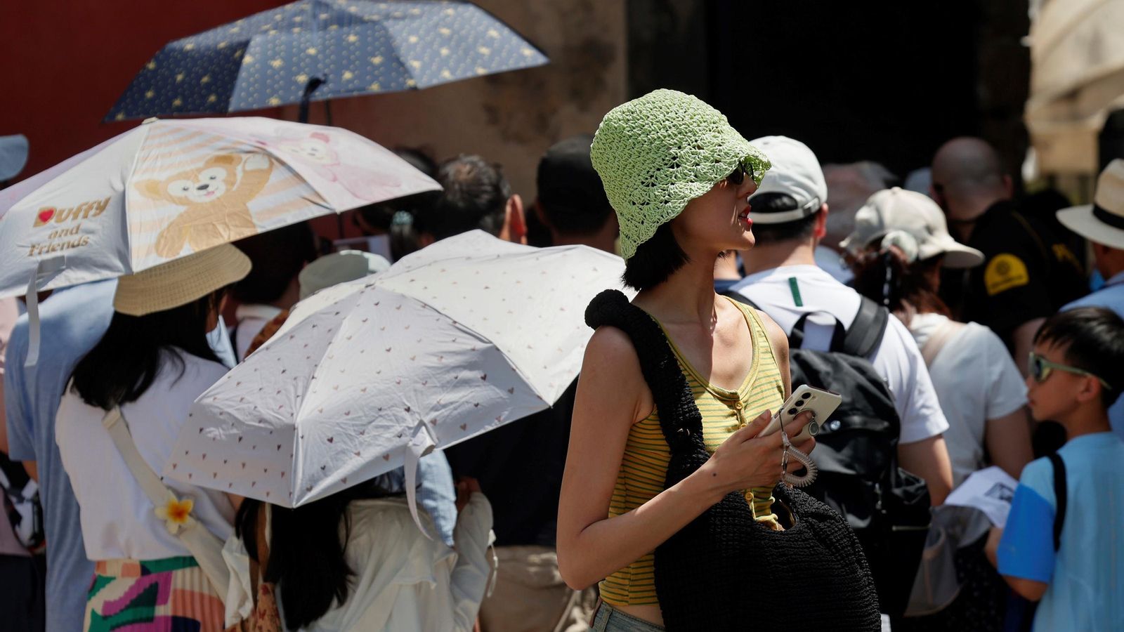 Un grupo de turistas, najo paraguas a modo de sombrillas, en la cola para visitar el Alcázar.