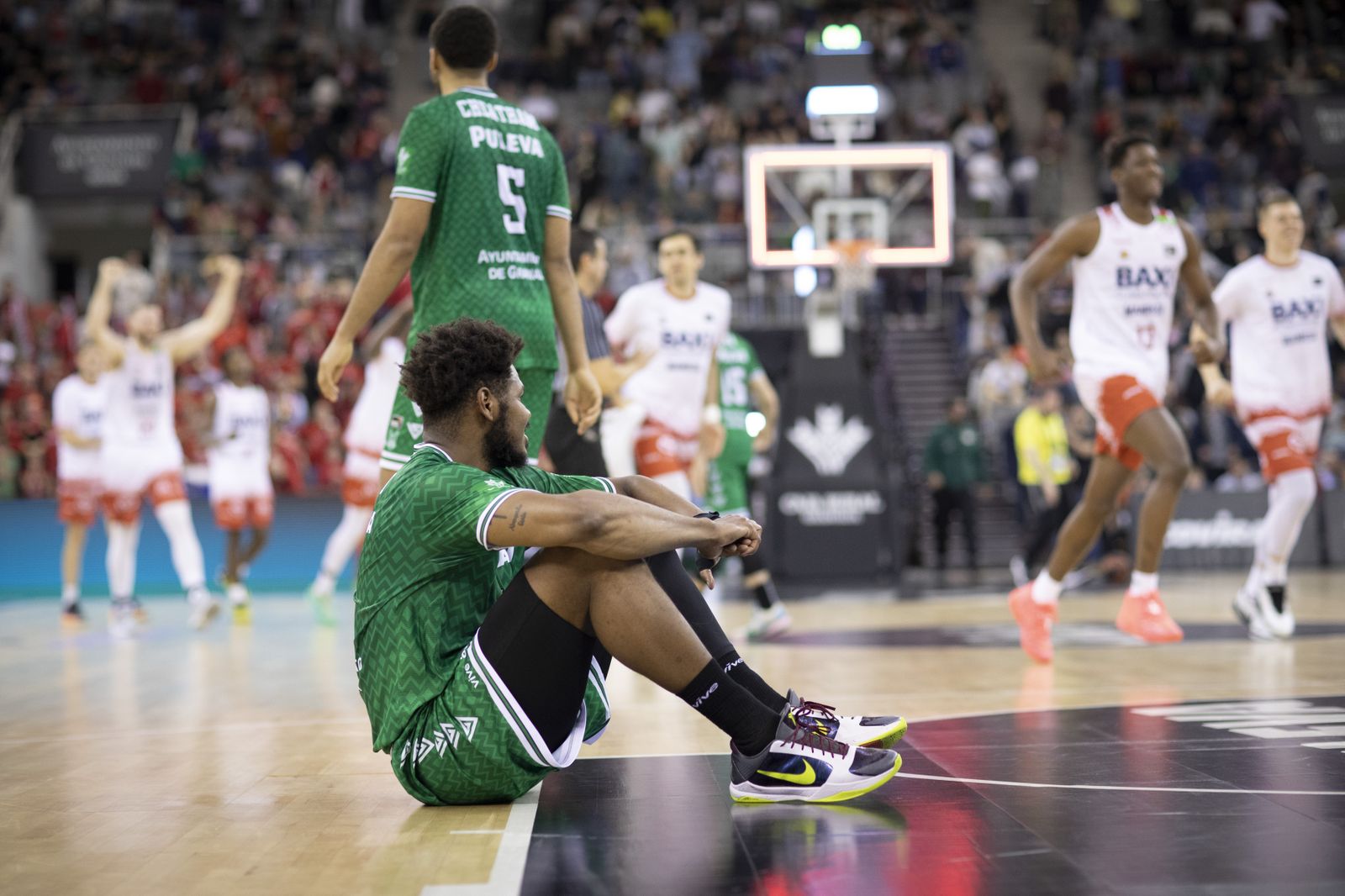 Cristiano Felicio, sentado en el parqué, con los jugadores de Manresa celebrando el trounfo de fondo.