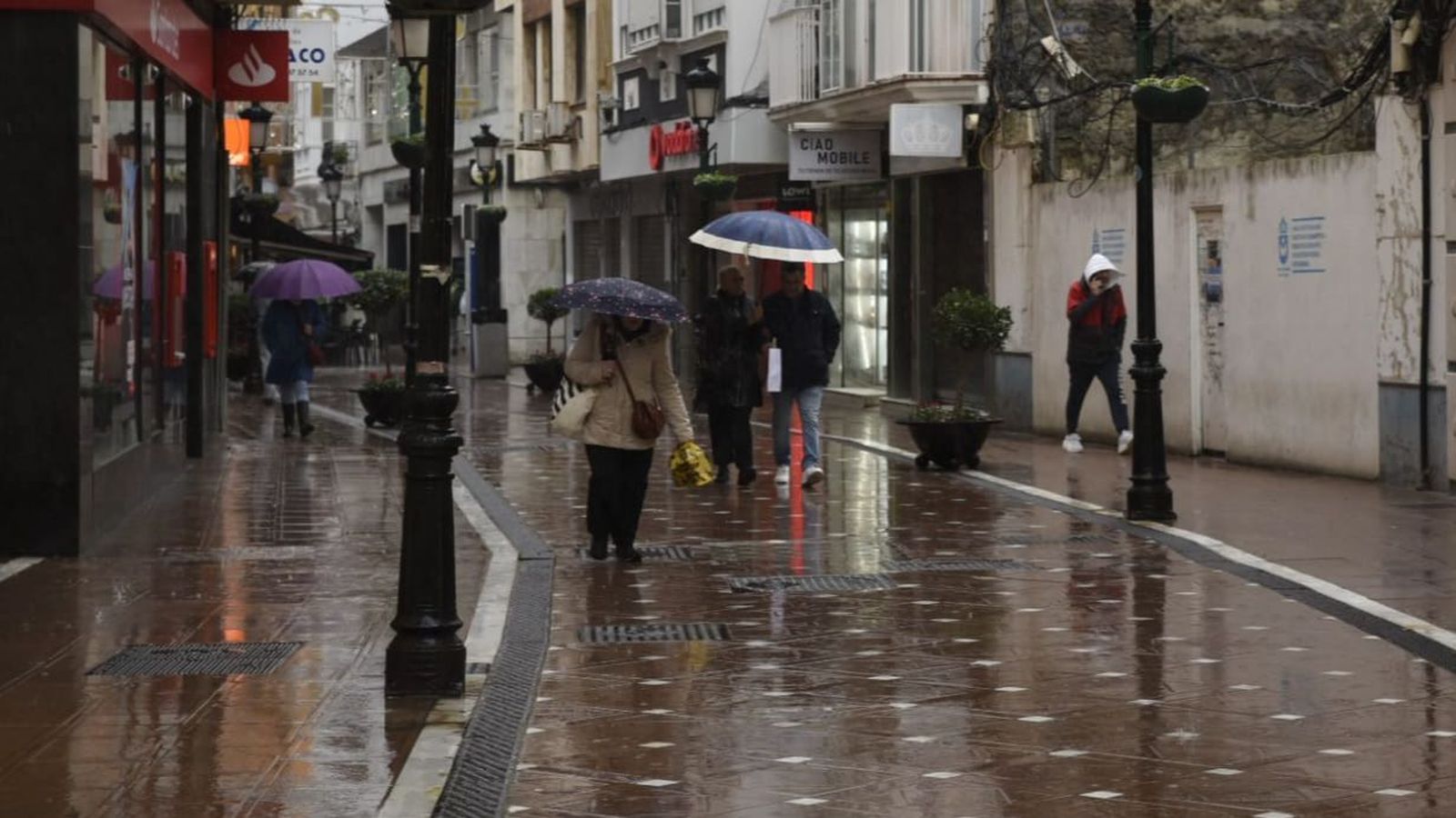 Ciudadanos pasean con paraguas por la calle Real de La Línea