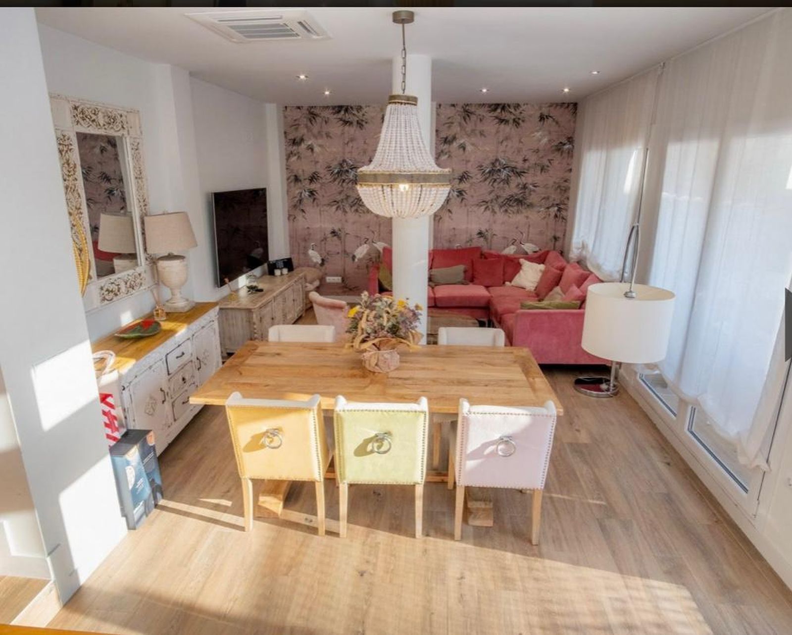 Salón-comedor. Un sofá de terciopelo color frambuesa, una mesa de comedor de roble y una lámpara de bronce y bolitas de madera decoran parte de la estancia.