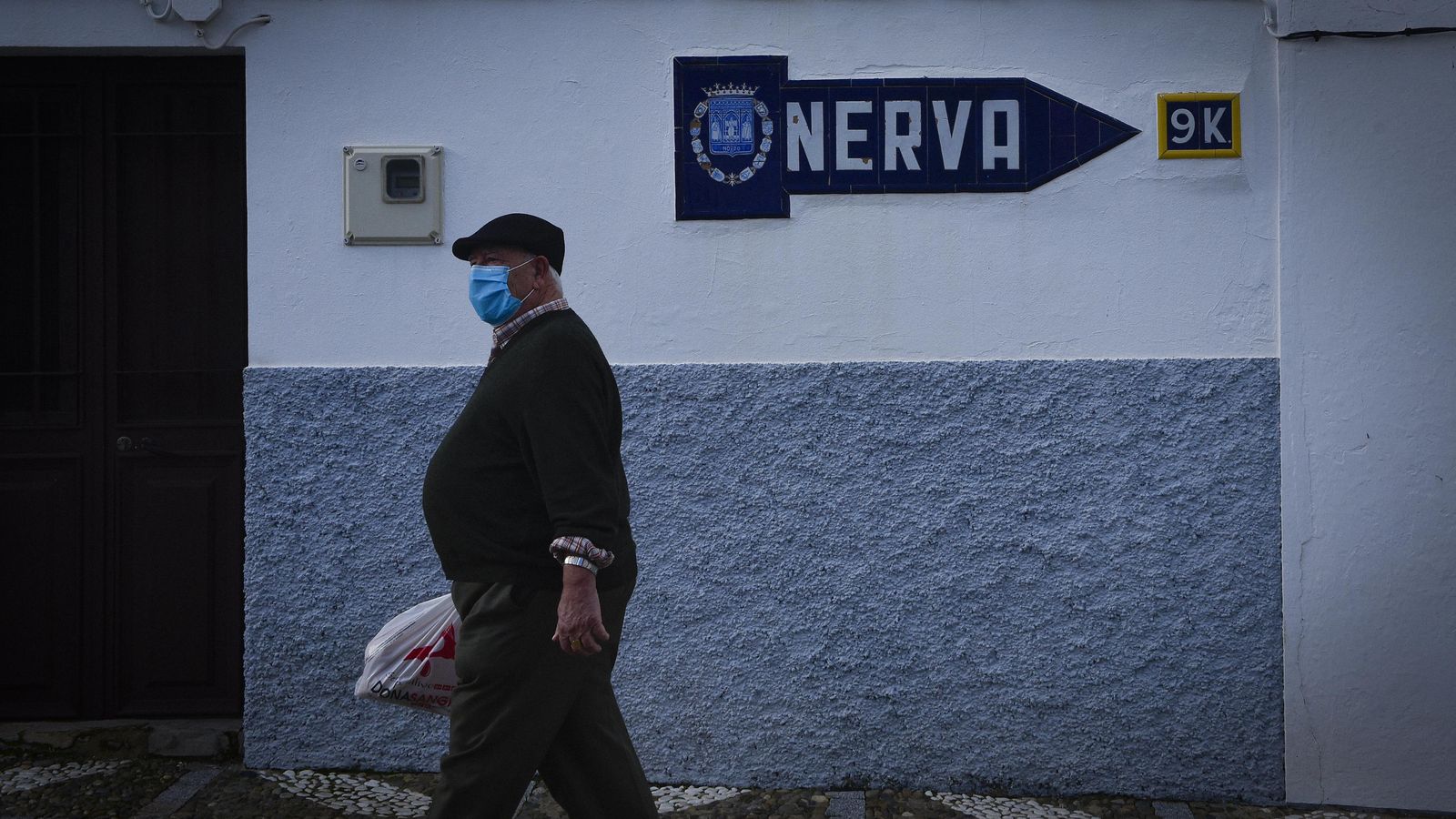 Un vecino con mascarilla pasa junto al cartel que indica la dirección y los 9 kilómetros que les separan de Nerva, donde sí ha habido casos.