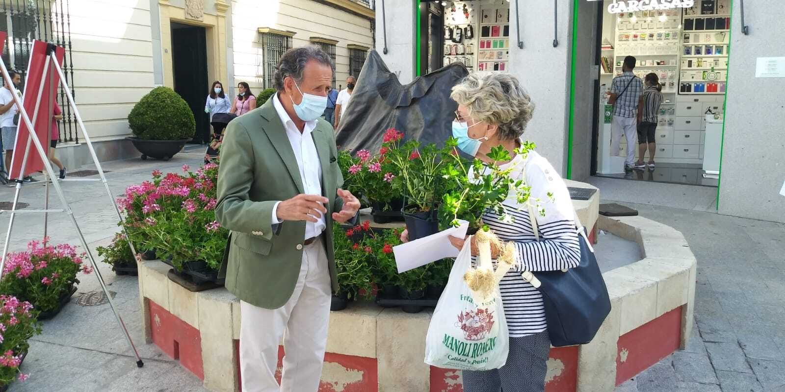 El alcalde, José María Román, entrega macetas de gitanillas a una ciudadana.
