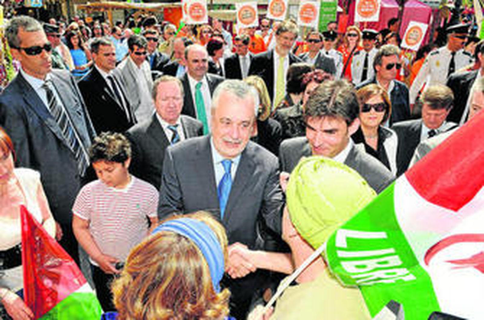 Griñán, ayer, en Santa Fe, saluda al público, con un grupo de protesta al fondo.