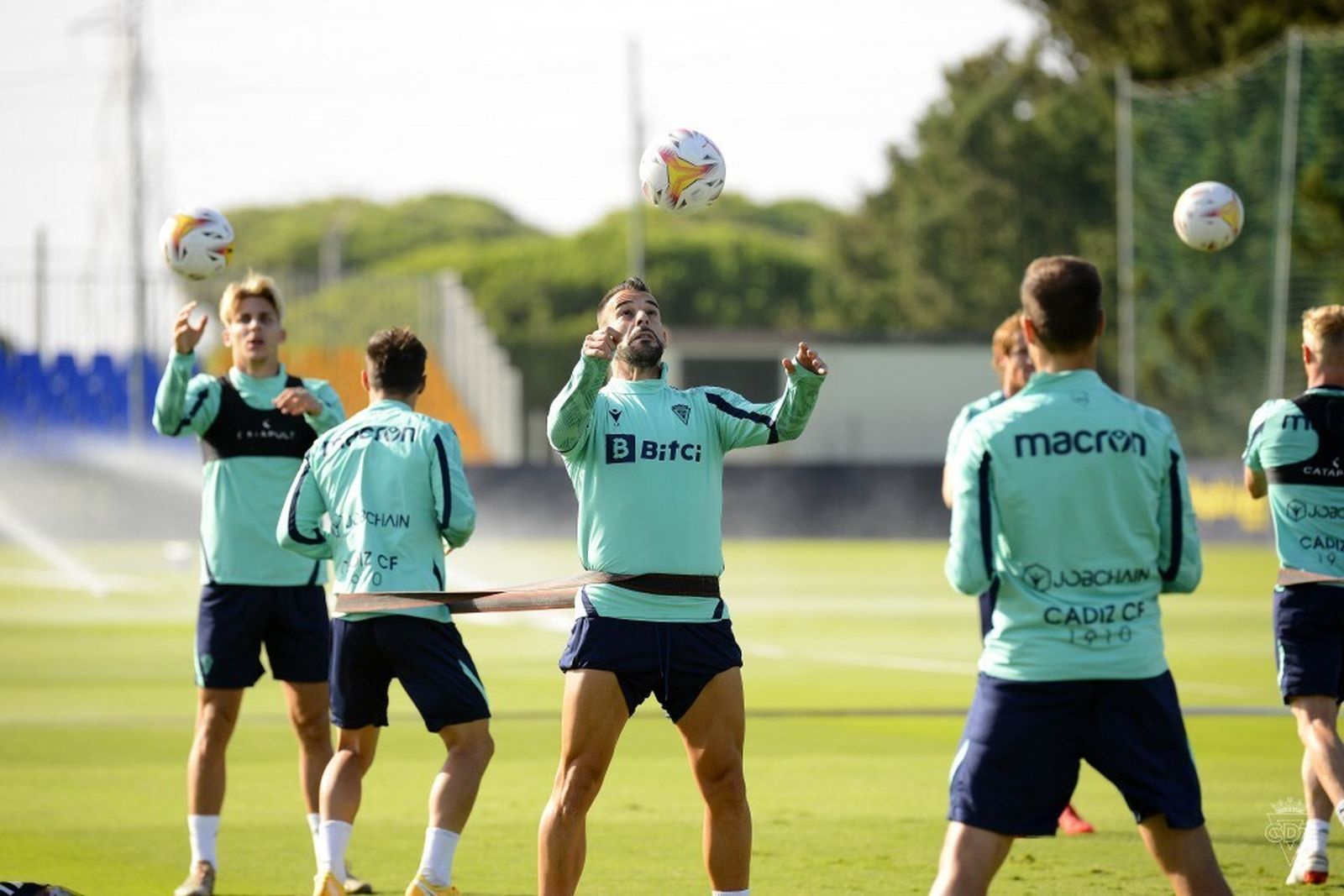 Negredo trata de conectar con el balón mientras está sujeto a un compañero por unos tensores.