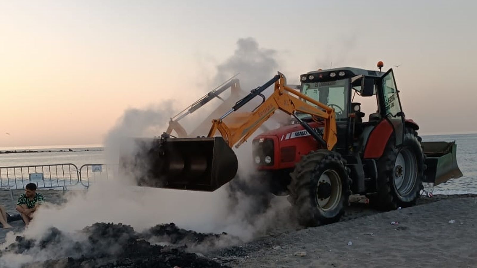 Un tractor retira restos de una hoguera.