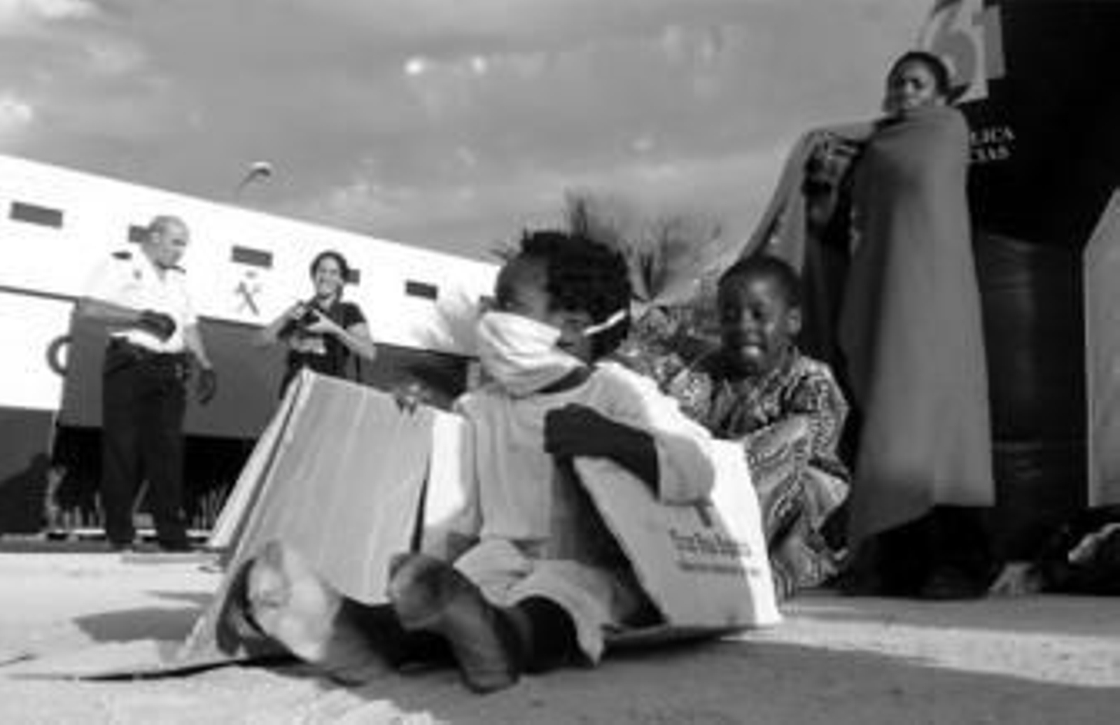 Dos de los menores que ayer llegaron a la playa isleña a bordo de la patera juegan con una caja de cartón de la Cruz Roja.