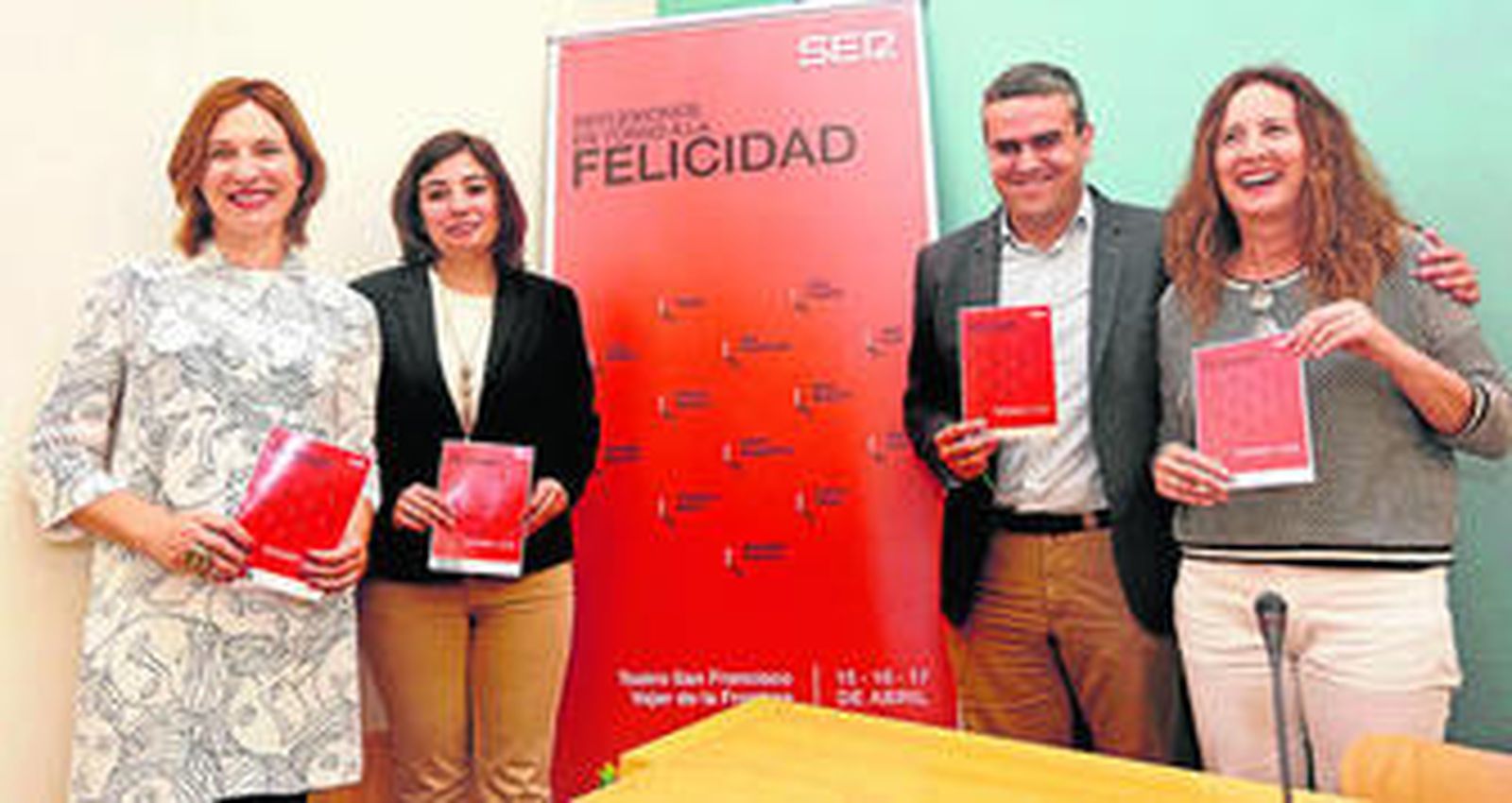 Lourdes Acosta, María Dolores Varo, José Ortiz y Remedios Palma, ante el cartel del 'Congreso del Bienestar. Reflexiones en torno a la felicidad'