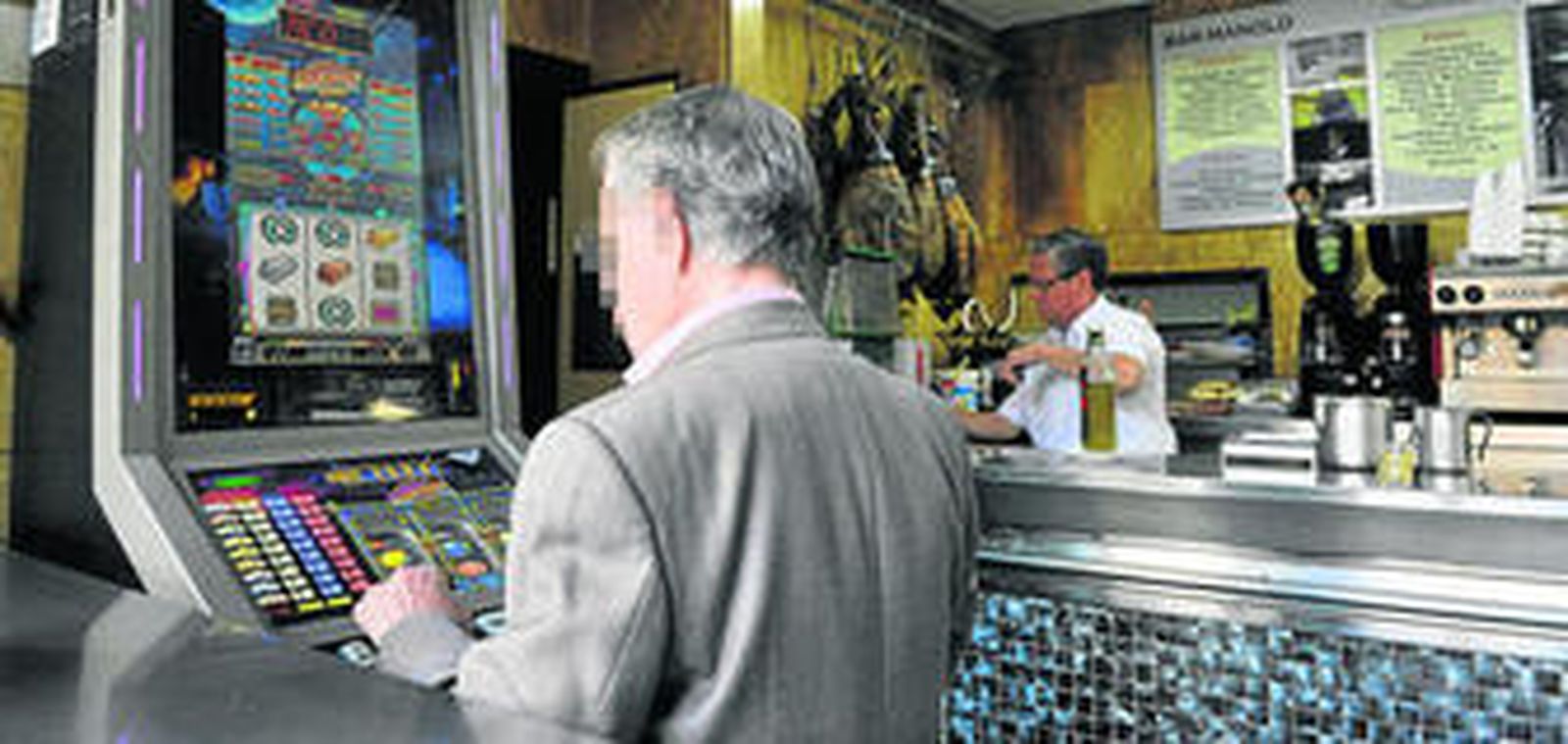 Un varón de edad media jugando a una máquina tragaperras en un bar sevillano.