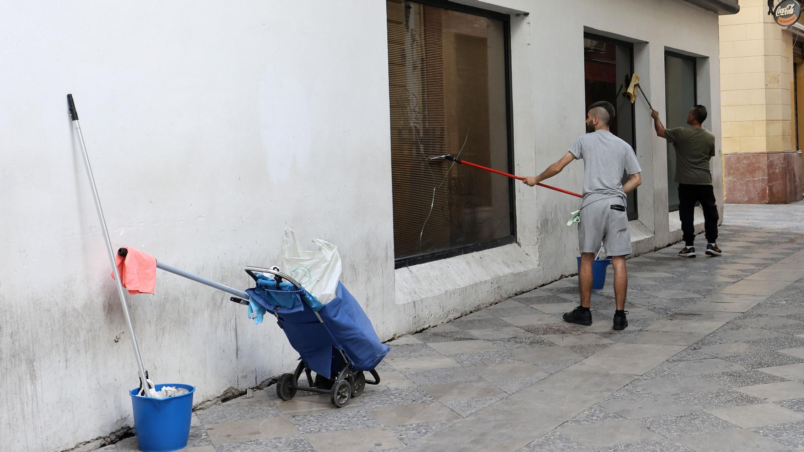 Dos trabajadores limpian los cristales de un establecimiento hostelero del centro.