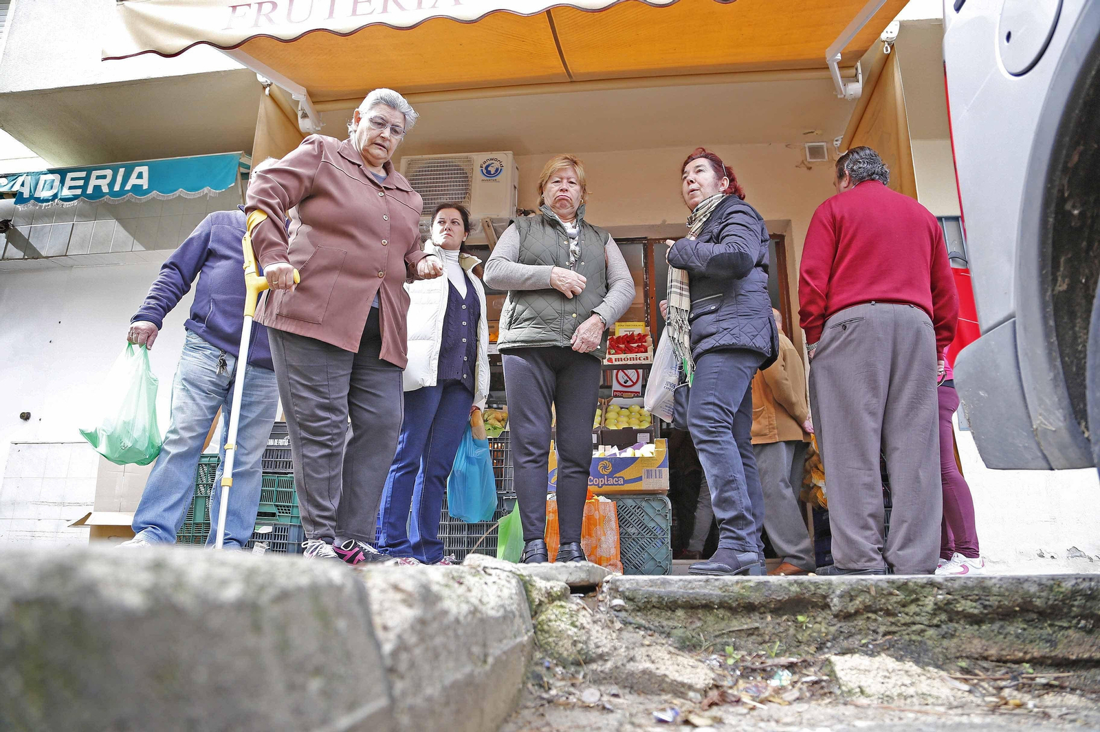 1. Varias vecinas del barrio señalan el lugar donde ya ha habido varias caídas. 2. El mal estado del acerado en las plazas es una de las principales quejas de los residentes.  3. Parque infantil inaugurado hace años y con el suelo aún de tierra.  4. Mosquitas en el techo de un bar a pesar de las tareas continuas de limpieza de su propietario.  5. La asociación de vecinos pide que se poden los árboles y se revisen. Esta palmera podría caerse, "al estar podrida", según le han trasladado a la presidenta vecinal. / REPORTAJE GRÁFICO: VANESA LOBO.