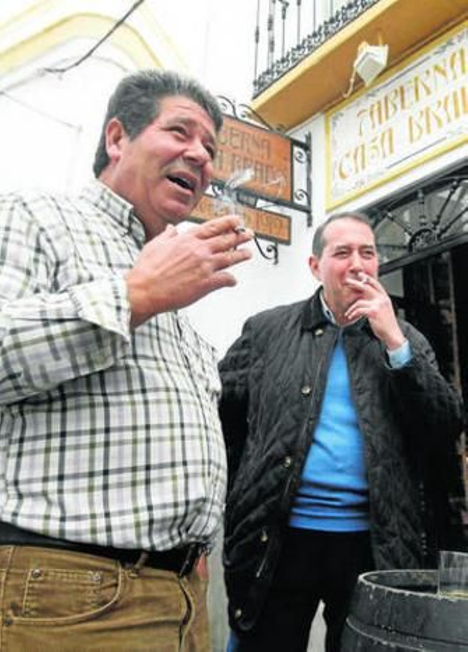 Dos hombres fuman en la puerta de una taberna.
