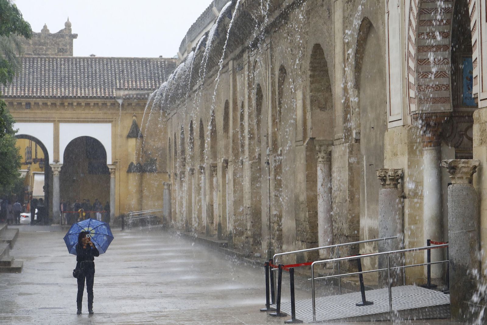 Una persona se protege de la lluvia en el Patio de los Naranjos de la Mezquita-Catedral.