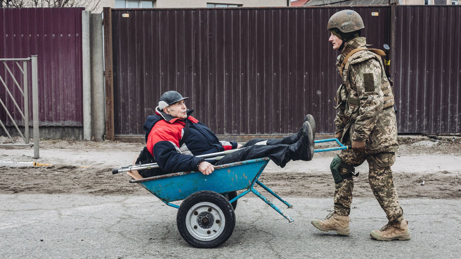 Un soldado ucraniano ayuda a un anciano llevándolo en una carretilla.